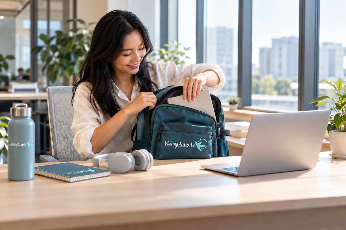 A new employee unpacking a branded teal backpack at a sunlit workstation.